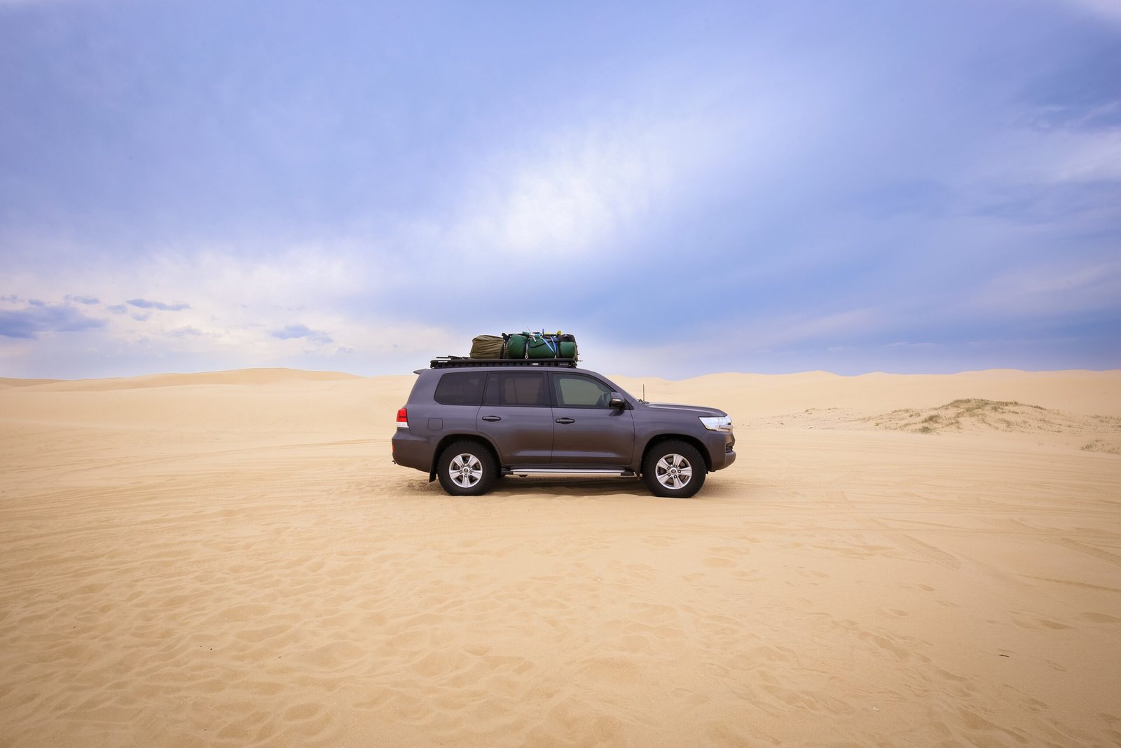 A car with baggage on top of it in the desert under a cloudy sky at daytime